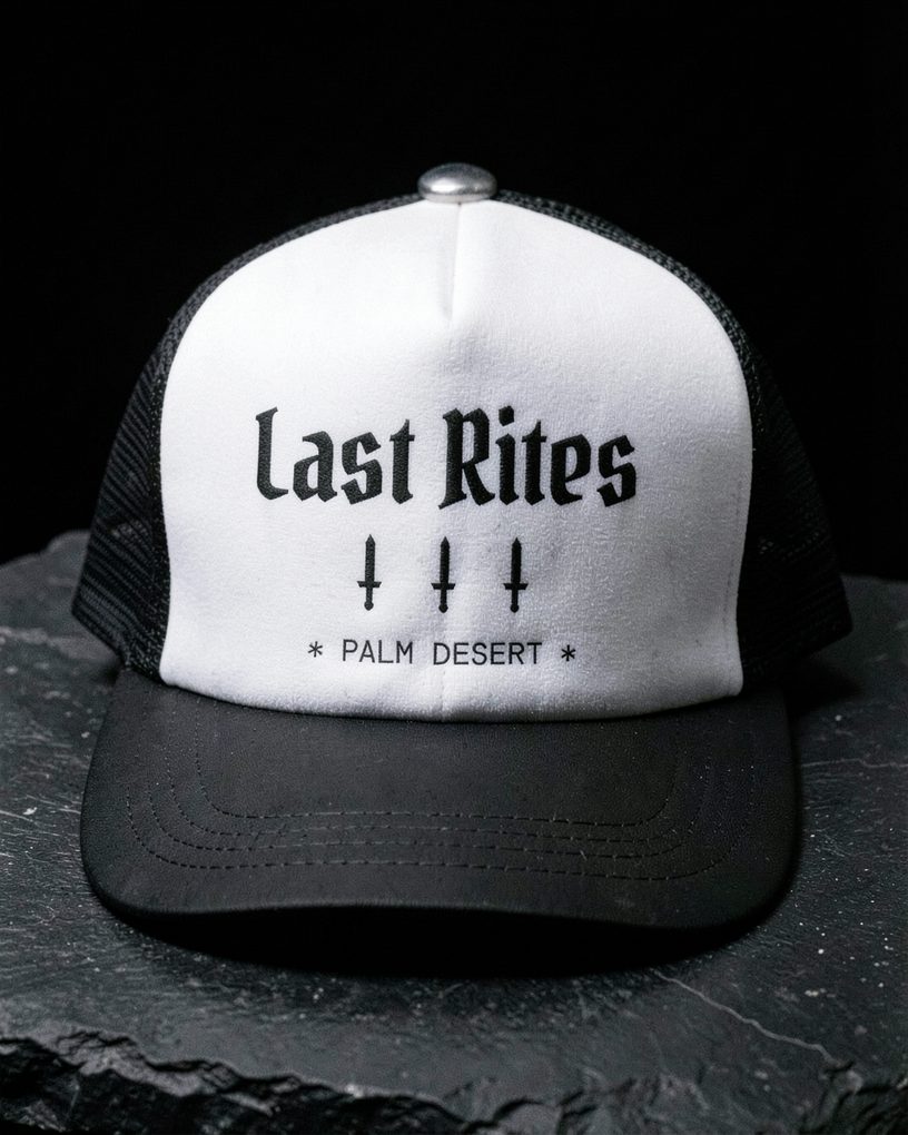 A trucker hat with a white foam front printed Last Rites, three daggers and Palm Desert, with a black mesh back and brim.