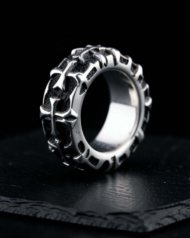 A wide sterling silver band ring with a raised row of gothic crosses around it, oxidised between them, on black slate.
