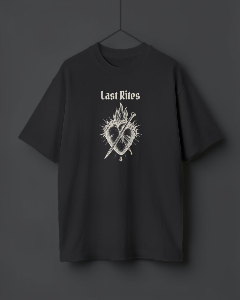 An oversized washed black tee hanging on a thread, printed in cream with Last Rites in gothic letters over a tattoo-flash sacred heart wrapped in thorns and flames, a dagger driven through it.